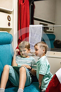 Two enthusiastic baby boy surfing internet on tablet on comfortable couch travel by train