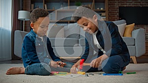 Two ethnic little boys African American multiracial kids schoolboys pupils children play game sitting on carpet in