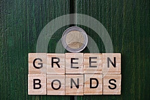 A two euro coin, above an inscription, green bonds, above a green, door. Investment concept for ecology by the European Union