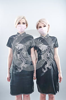 Two European-looking women are dressed in black Chinese dresses and medical face masks. blonde girls do not keep a safe distance