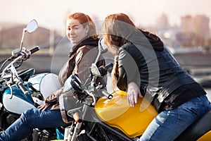 Two European women motorcyclists talking cheerfully while sitting on their motorcycles