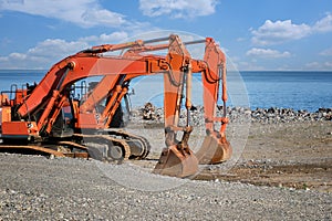 Two excavators with lowered buckets stand on the seashore