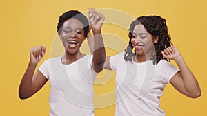 Two excited african american women dancing under money shower, enjoying successful deal, orange background
