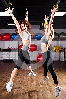 Two excited fitness girls jumping in health center