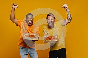 Two excited men screaming and gesturing with thrill holding pizza while standing isolated