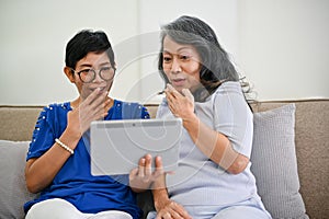 Two excited middle-aged women are watching something exciting online through a tablet