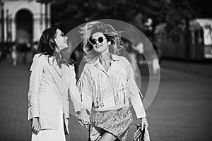 Two excited women walking on street. Gorgeous girl holding hands with friend while walking around city. Outdoor portrait