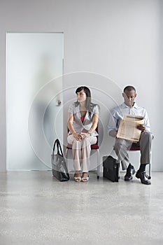 Two Executives Sitting On Chairs In Corridor BY Open Door