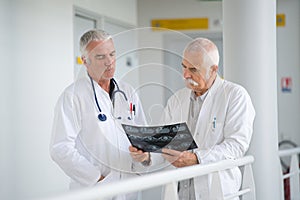 Two experienced male doctors discussing x-rays in hospital corridorb