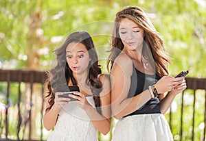 Two Expressive Mixed Race Girlfriends Texting on Their Smartphones