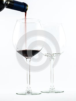 Two exquisite transparent glasses with red wine and a bottle pouring wine on a white background