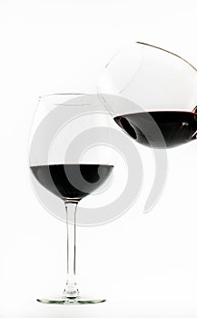 Two exquisite transparent glasses with red wine - one pouring wine into the other - on a white background