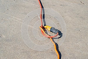 Two extension cords plugged into each other with a knot on a cement background