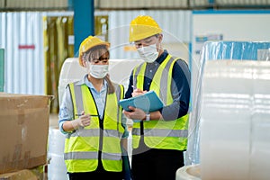 Two factory workers with hygiene mask discuss together to manage the product in warehouse workplace