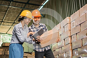 two factory workers using a tablet and carrying cardboard boxes