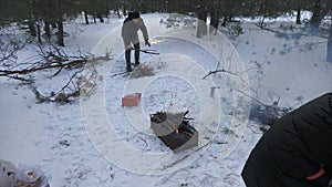 Two families grill kebabs in winter in a snowy pine forest.