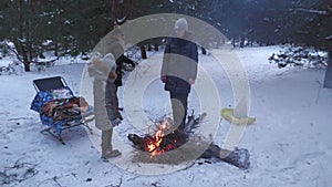 Two families grill kebabs in winter in a snowy pine forest.