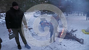 Two families grill kebabs in winter in a snowy pine forest.