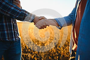 Two farmers shaking hands in soybean field.