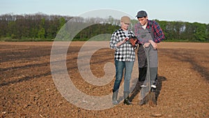 Two farmers stand in a field, communicate, use a tablet