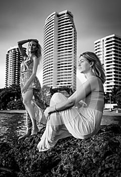 Two fashion models posing in red and turquoise dresses in the rays of the setting sun on tropical beach on a background