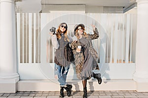Two fashionable joyful smiling girls having fun on sunny street in city. Stylish look, travelling together, wearing