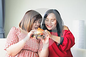 Two fat women in Asians eat large hamburgers.