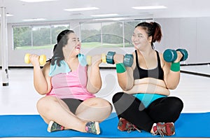 Two fat women with dumbbells on the mat