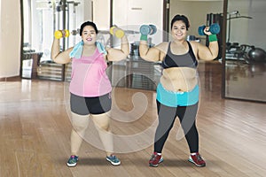 Two fat women lifting dumbbells in sport center