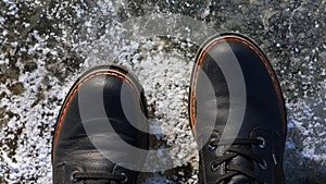 Two feet with black boots are standing on the ice. Top view. Winter concept.