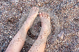 Child Legs On The Beach Full Of Small Pebbles On A Summer Day.