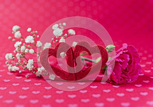 Two felt hearts with carnation and white flowers on romantic heart patterned background