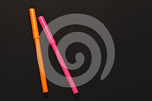 Two felt-tip pens of pink and orange colors on black paper background