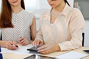Two female accountants counting on calculator income for tax form completion hands closeup. Internal Revenue Service