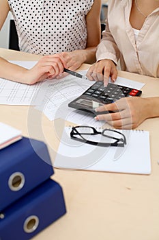 Two female accountants counting on calculator income for tax form completion hands closeup. Internal Revenue Service