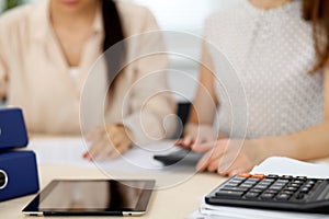 Two female accountants counting on calculator income for tax form completion hands closeup. Internal Revenue Service