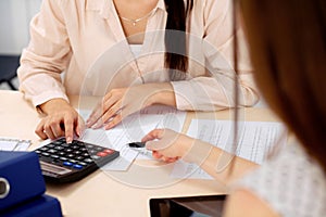 Two female accountants counting on calculator income for tax form completion hands closeup. Internal Revenue Service