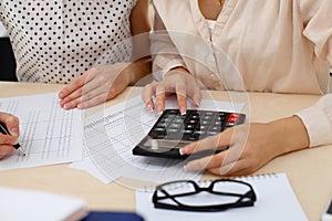 Two female accountants counting on calculator income for tax form completion hands closeup. Internal Revenue Service