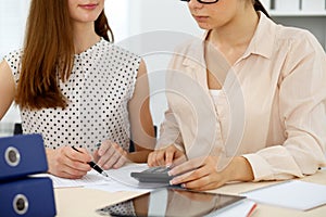 Two female accountants counting on calculator income for tax form completion hands closeup. Internal Revenue Service