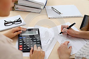 Two female accountants counting on calculator income for tax form completion hands closeup. Internal Revenue Service