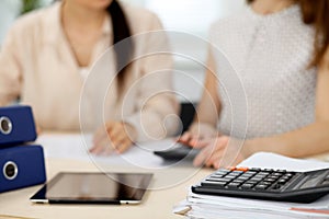 Two female accountants counting on calculator income for tax form completion hands closeup. Internal Revenue Service