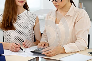 Two female accountants counting on calculator income for tax form completion hands closeup. Internal Revenue Service