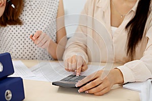 Two female accountants counting on calculator income for tax form completion hands closeup. Internal Revenue Service