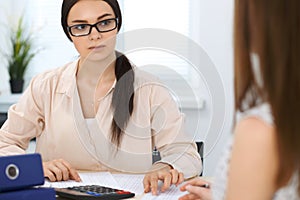 Two female accountants counting on calculator income for tax form completion hands closeup. Internal Revenue Service