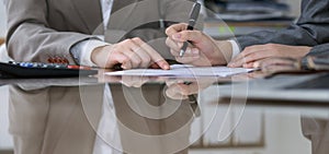 Two female accountants counting on calculator income for tax form completion, hands closeup. Internal Revenue Service