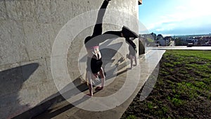 Two female acrobat performs handstand on the wall at sunset outdoors