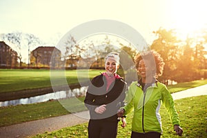 Two female athletes running in sunny park