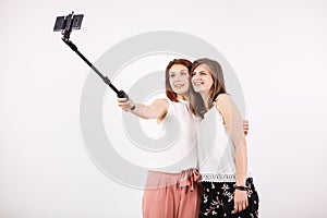 Two female best friends having a lot of fun while taking a selfie with a selfie stick