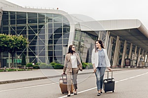 Two female co-workers returning from a joint business trip. Young women in business clothes with suitcases on the street