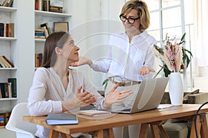Two female collegues working with laptop and discussing new project photo